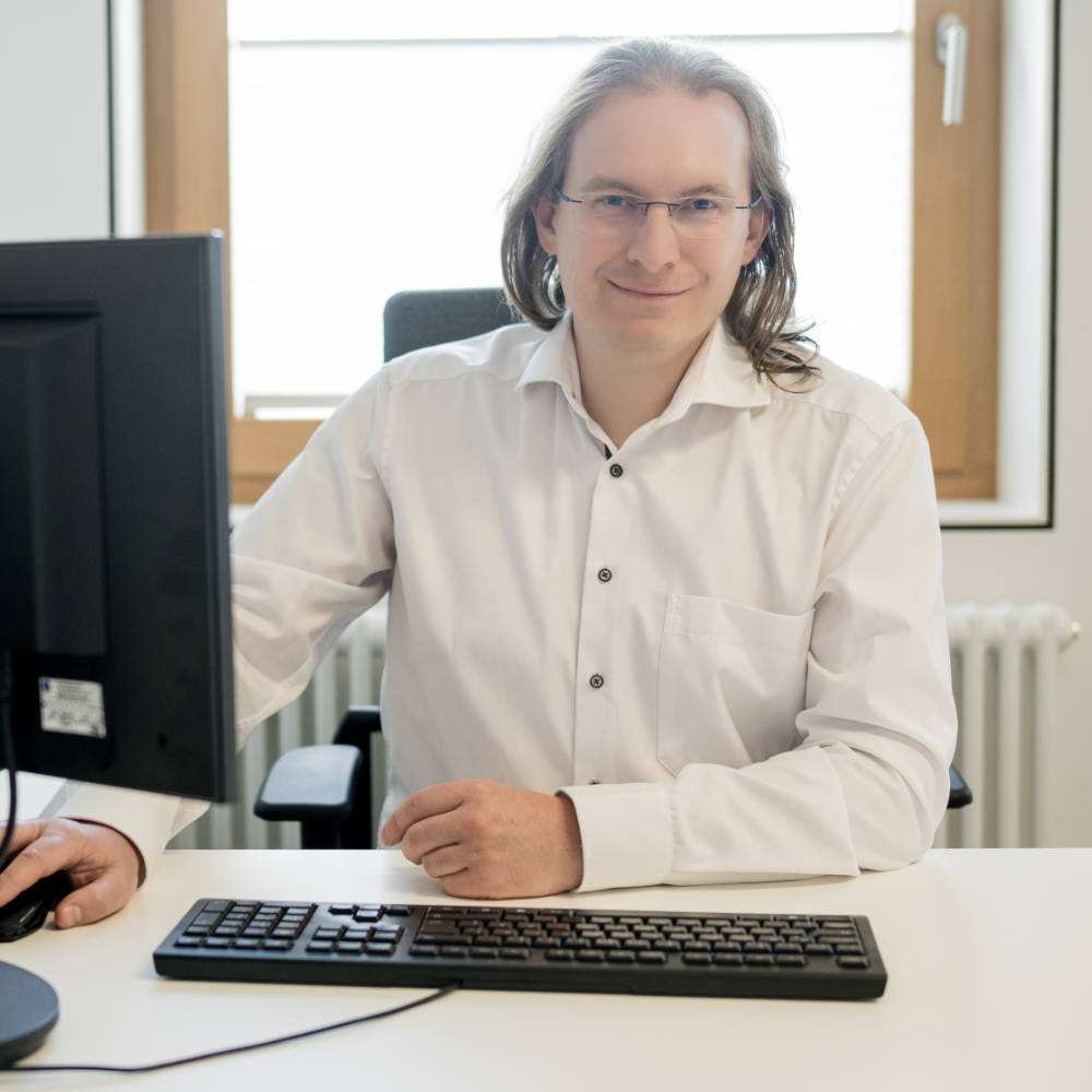 Porträt Dr. med. Marc Morgott an einem Schreibtisch mit Hand auf der Maus